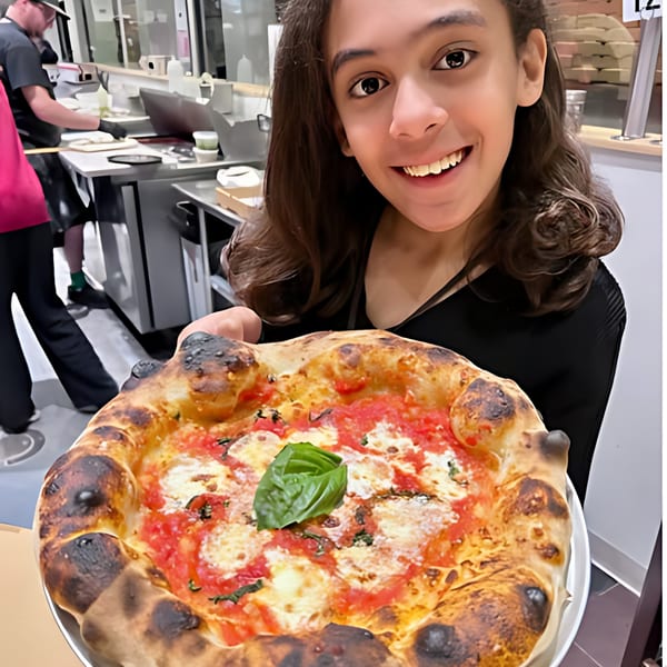 Smiling person holding a freshly baked Rodrigo's Craft Pizza with basil, cheese, and tomato sauce.