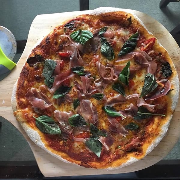 Rodrigo's Craft Pizza with prosciutto, fresh basil, and tomatoes on a wooden peel.