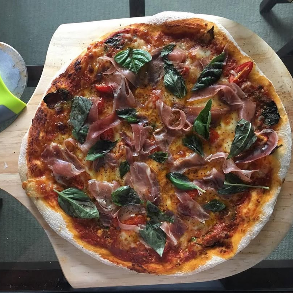 Rodrigo's Craft Pizza with prosciutto, fresh basil, and tomatoes on a wooden peel.