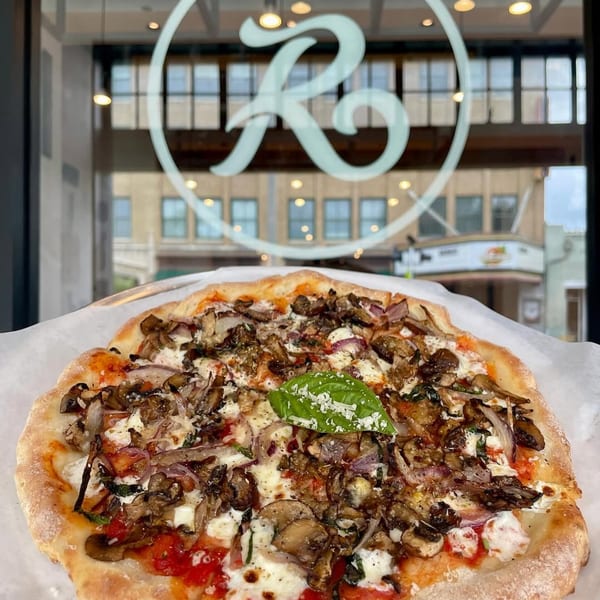 A mushroom and onion pizza with a basil leaf and cheese, in front of a window with the Rodrigo's logo.