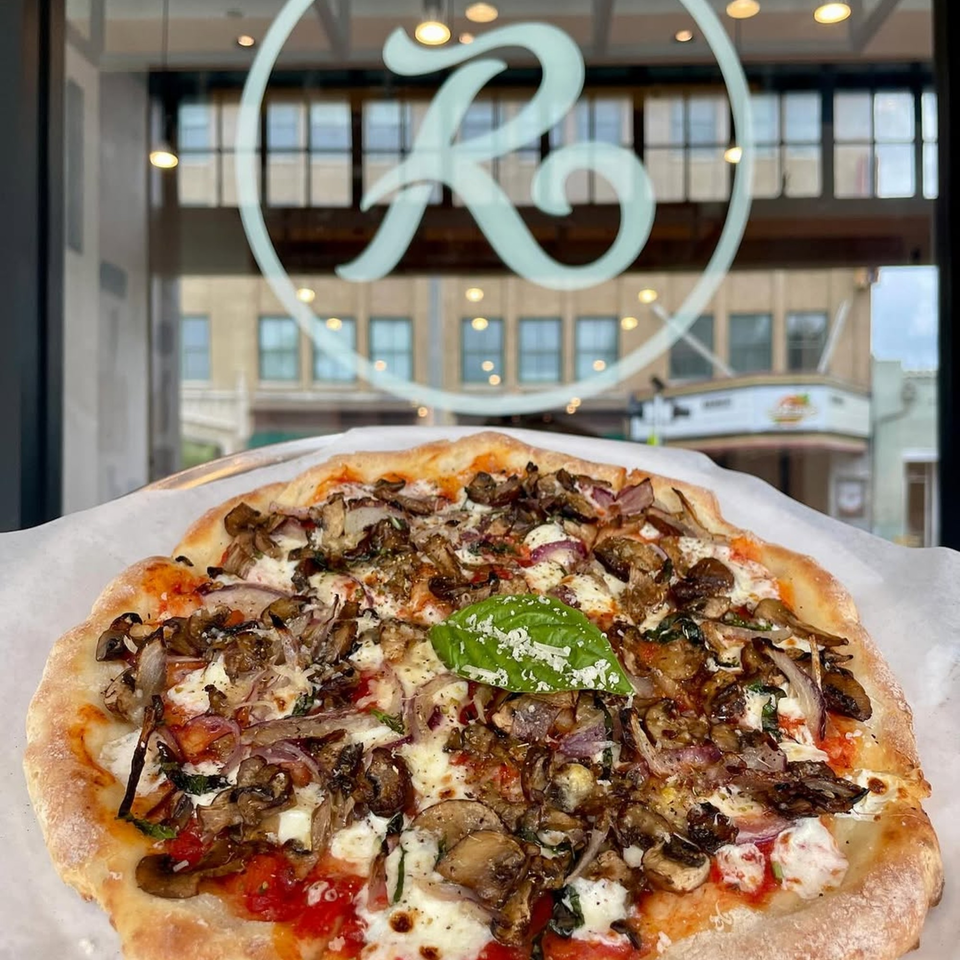 A mushroom and onion pizza with a basil leaf and cheese, in front of a window with the Rodrigo's logo.