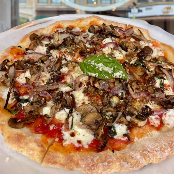 A whole mushroom and red onion pizza from Rodrigo's Craft Pizza, topped with fresh basil and cheese.