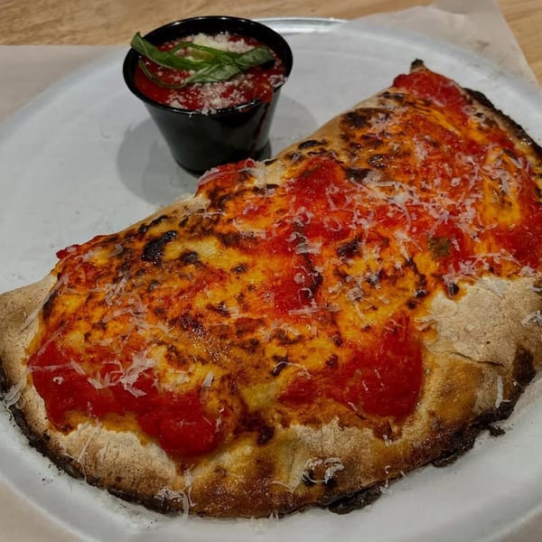 A Rodrigo's Craft Pizza calzone, topped with red sauce and parmesan, served with a side of marinara.