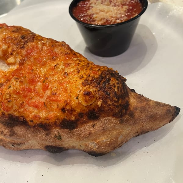 A golden-brown calzone with melted cheese and tomato sauce, served with a side of marinara.