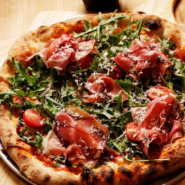 A Rodrigo's Craft Pizza with prosciutto, arugula, cherry tomatoes, parmesan, and balsamic glaze.