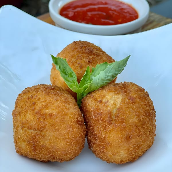 Three golden-brown arancini balls with a fresh basil leaf, served with a side of red marinara sauce.