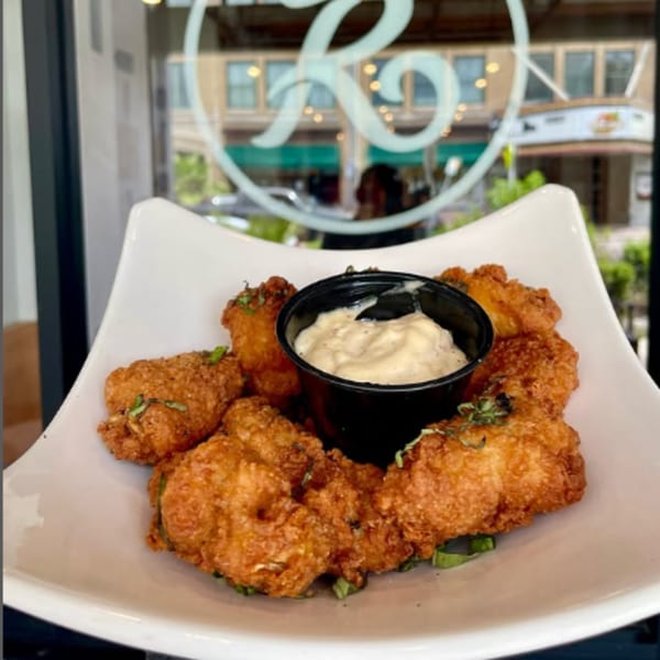 Golden-brown fried appetizers with a side of creamy dipping sauce on a white plate at Rodrigo's Craft Pizza.