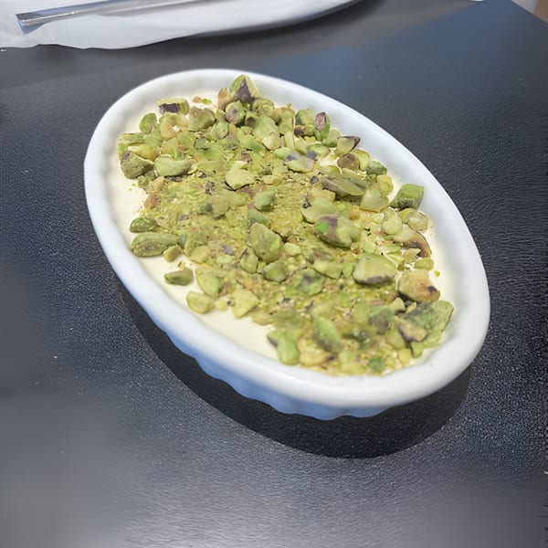 A white oval dish filled with a creamy dessert topped with chopped pistachios on a dark table.